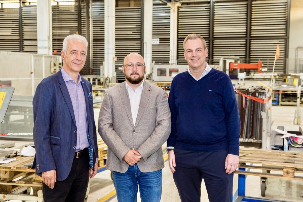 Three men standing in an industrial facility, posing for a group photo with equipment and machinery in the background.