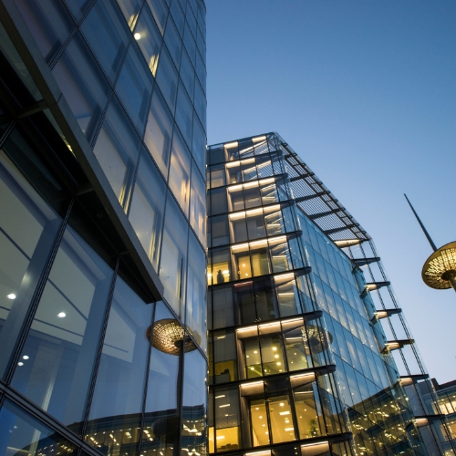 Glass-covered modern office building illuminated from within during dusk, showcasing sleek architecture and a professional atmosphere.